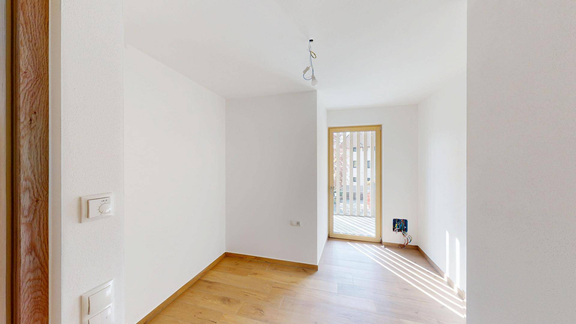 Kleineres Zimmer mit Holzboden und einer Tür, die zu einem Außenbereich führt.