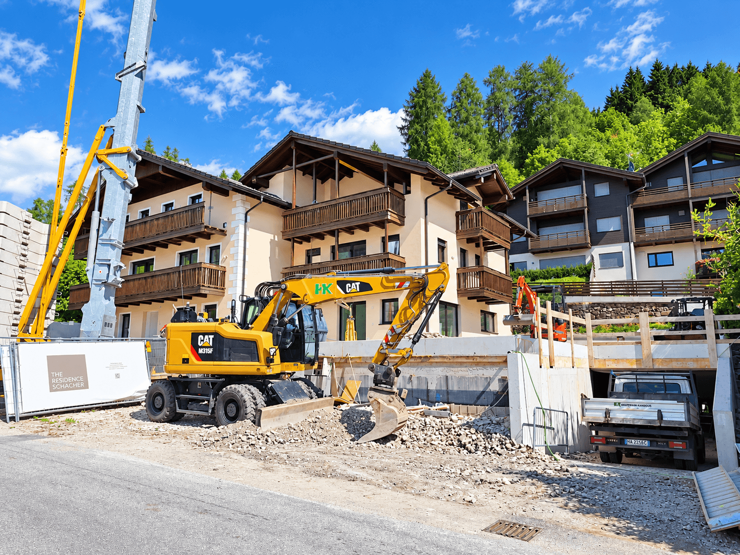 Neubau im alpinen Stil mit Balkonen, umgeben von Baustelle und grüner Berglandschaft.