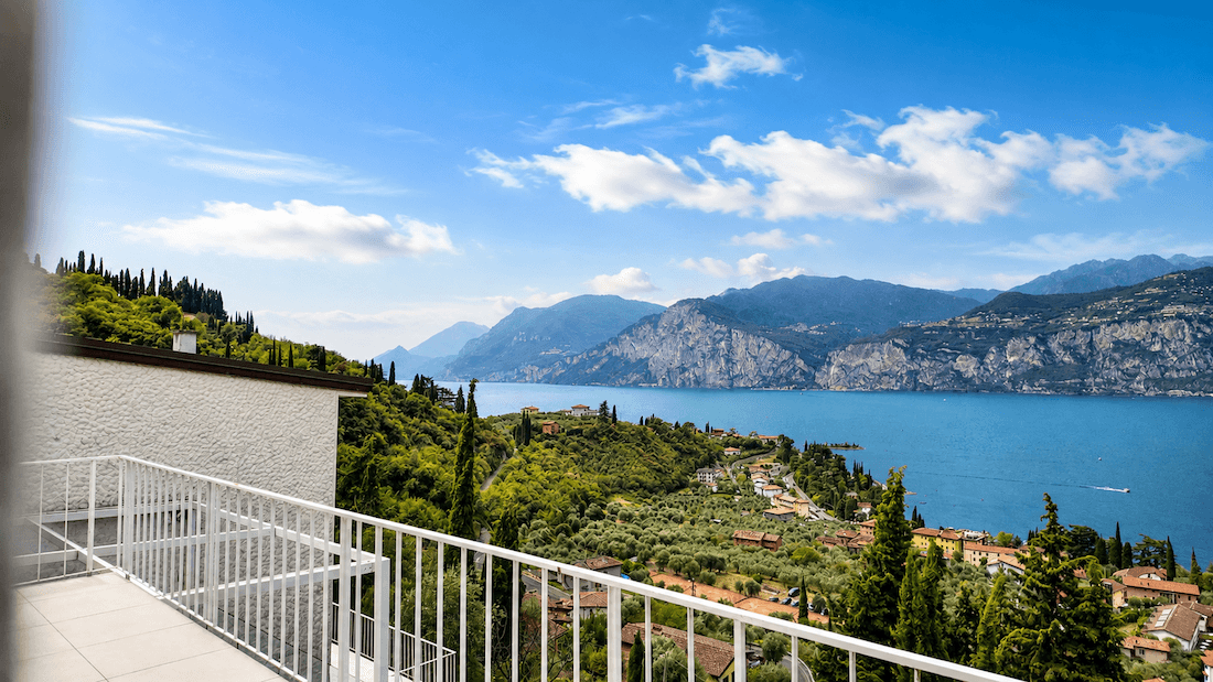 Balkon mit weißen Geländern und einem beeindruckenden Panoramablick auf den See, die Berge und die grüne Umgebung.