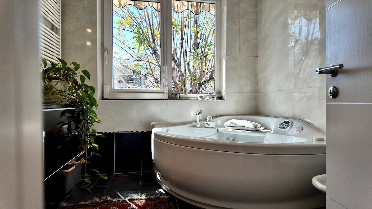 Badezimmer mit Eckbadewanne, Fenster und dunklen Fliesen.