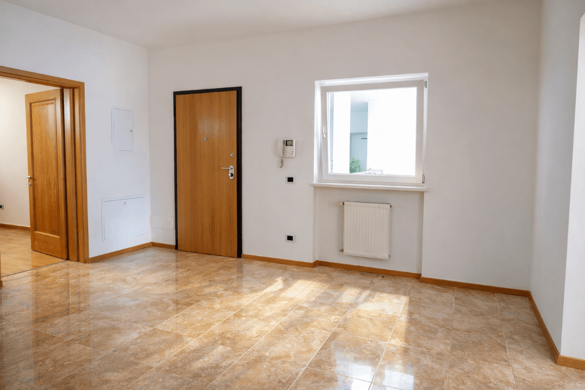 Leerer Eingangsbereich mit glänzenden Fliesen, weiß gestrichenen Wänden und Fenster.