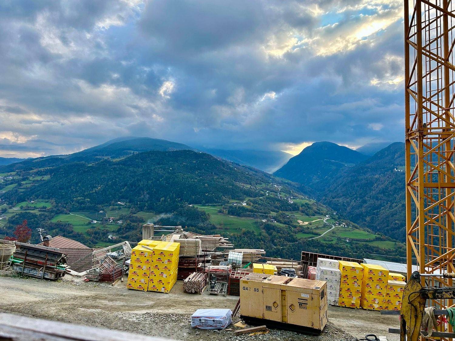 Baumaterialien auf einer Baustelle mit weitem Blick auf die umliegende Bergwelt unter dramatischem Himmel.