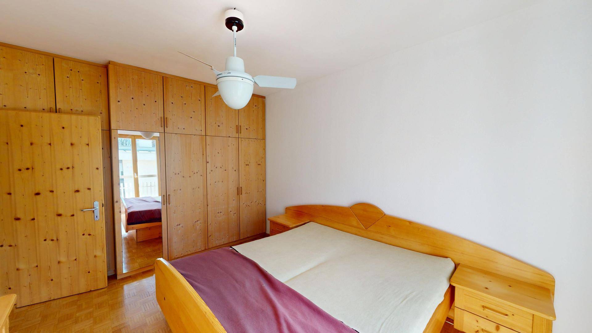 Helles Schlafzimmer mit großen Holzschränken, Holzbett und Deckenventilator.