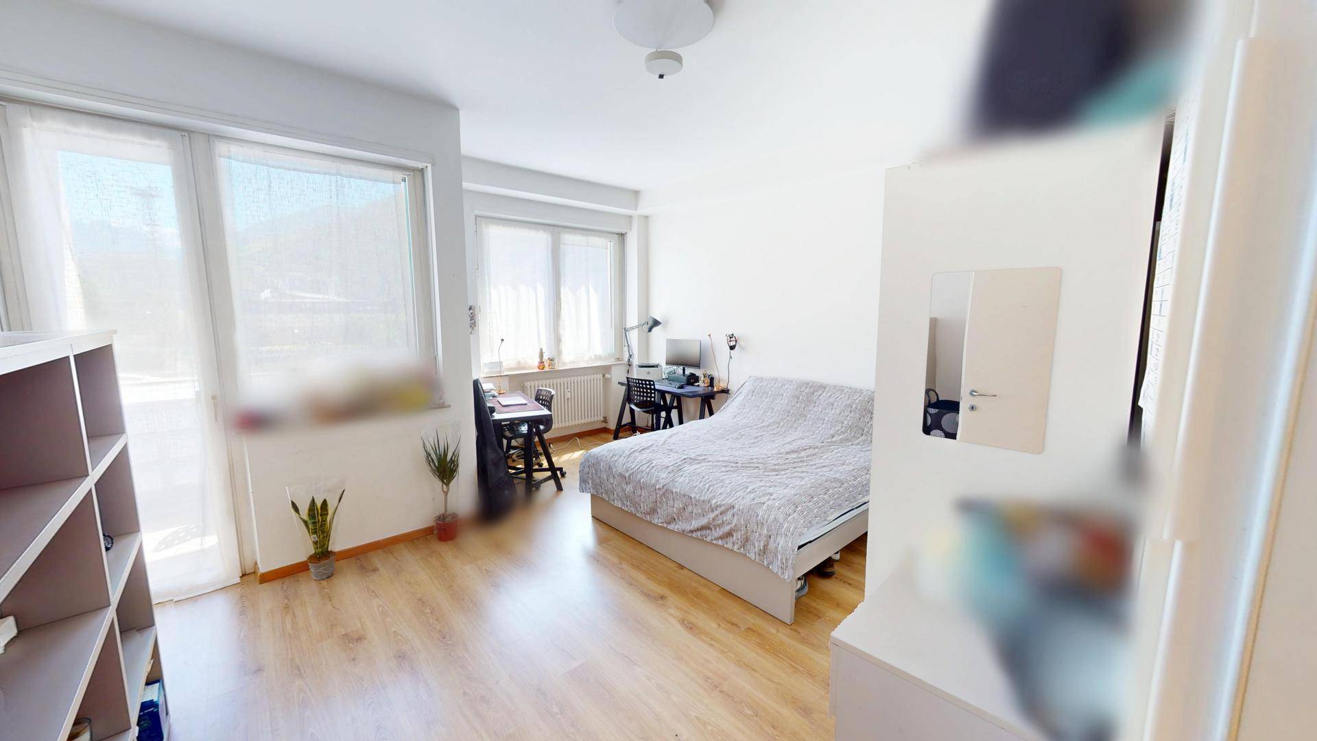 Schlafzimmer mit Holzboden, Doppelbett und Schreibtischbereich am Fenster.