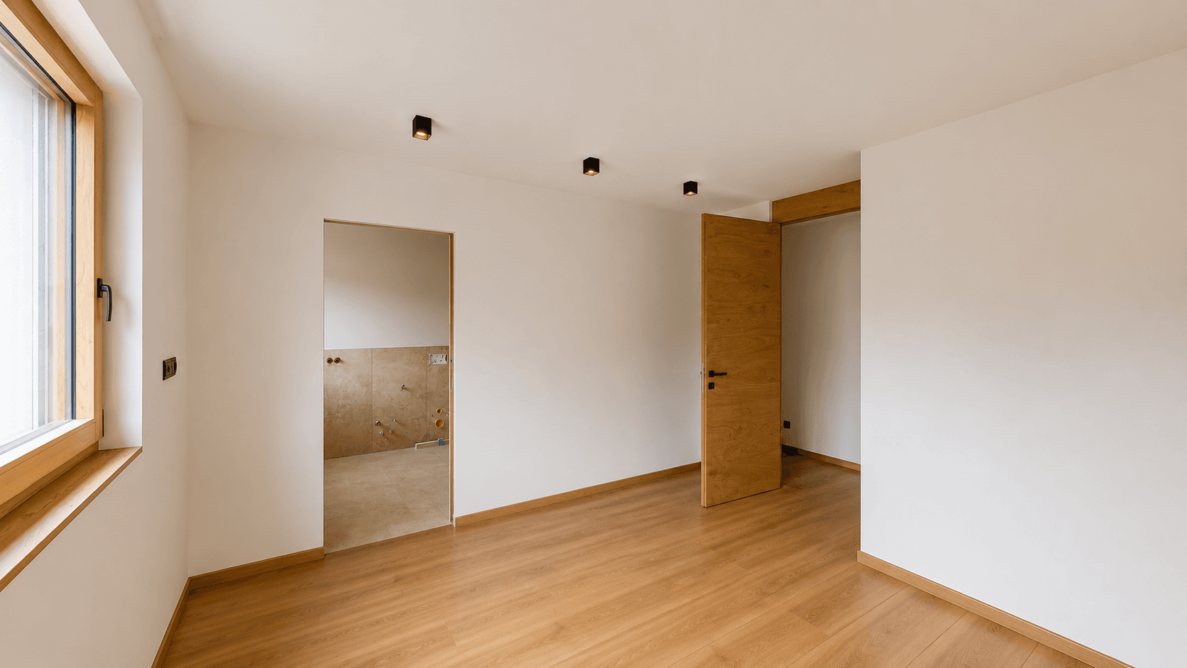 Helles Zimmer mit Holzboden und Zugang zu einem Badezimmer im Rohbauzustand.