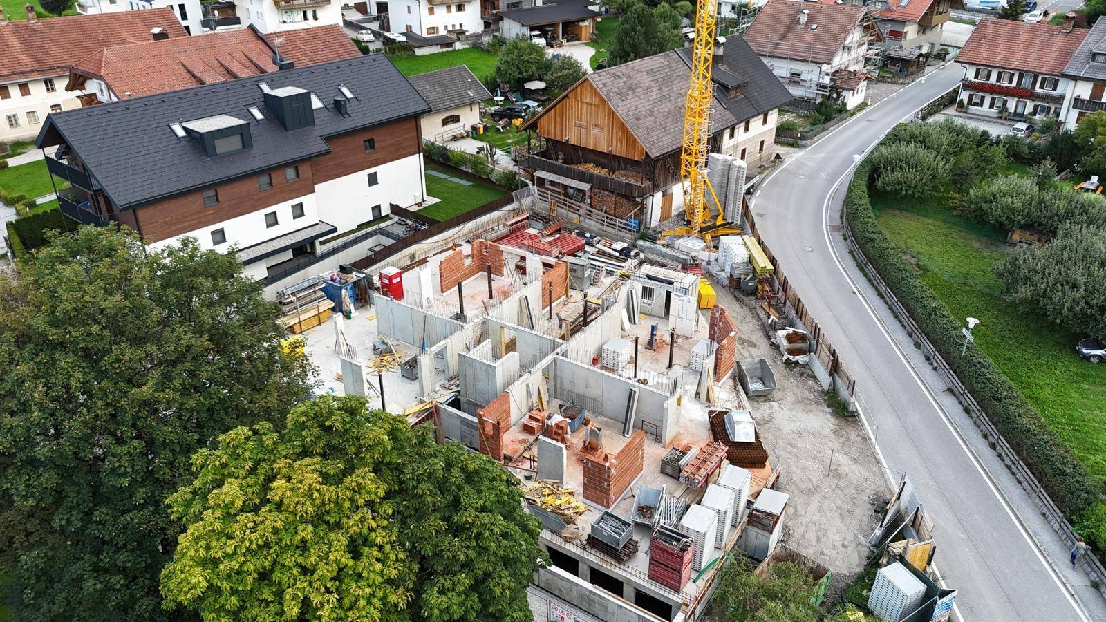 Luftaufnahme einer Baustelle mit im Bau befindlichem Gebäude, umgeben von Wohnhäusern und einer Straße.