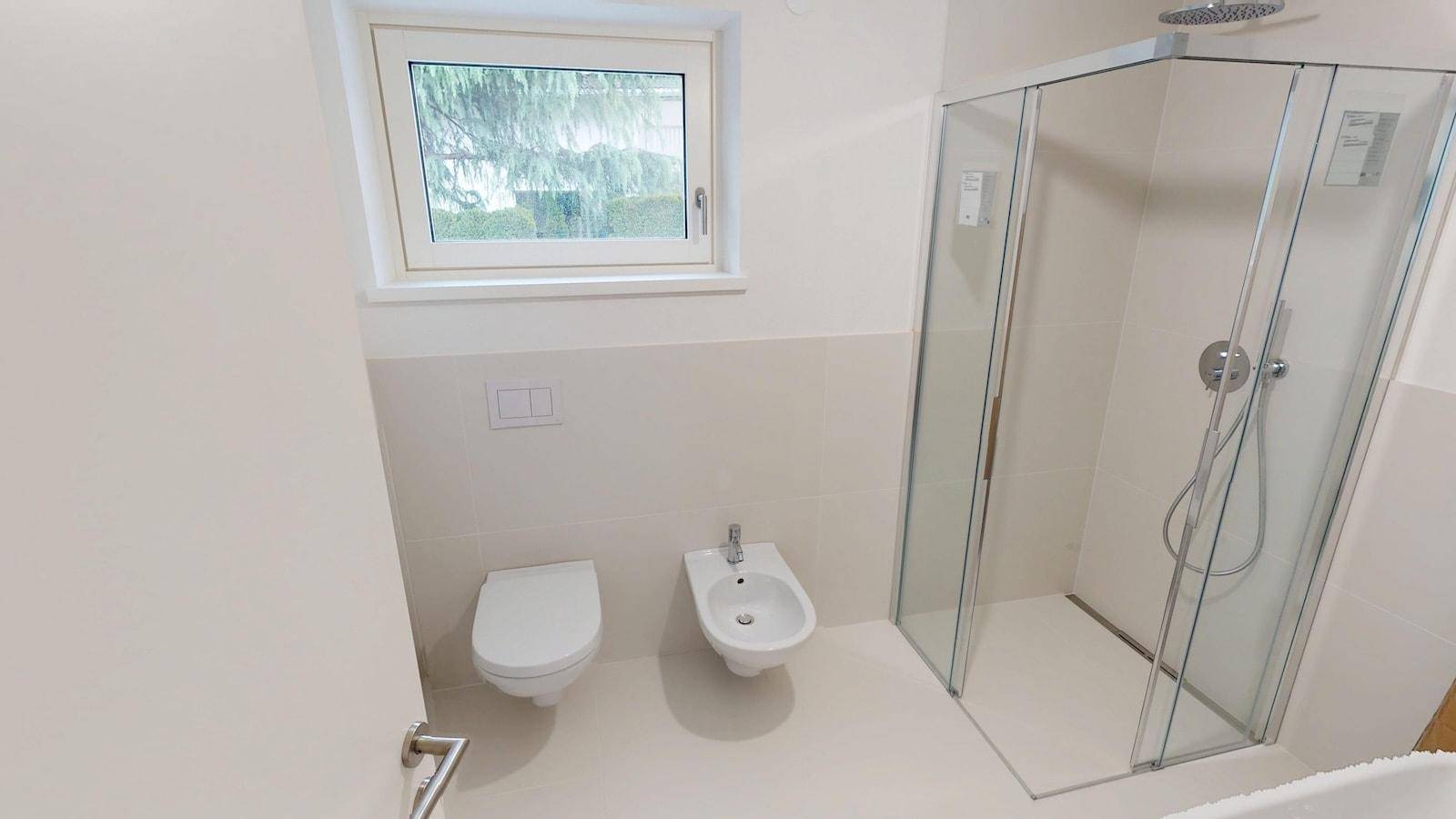 Modernes Badezimmer mit Dusche, WC, Bidet und einem Fenster für natürliche Belüftung.