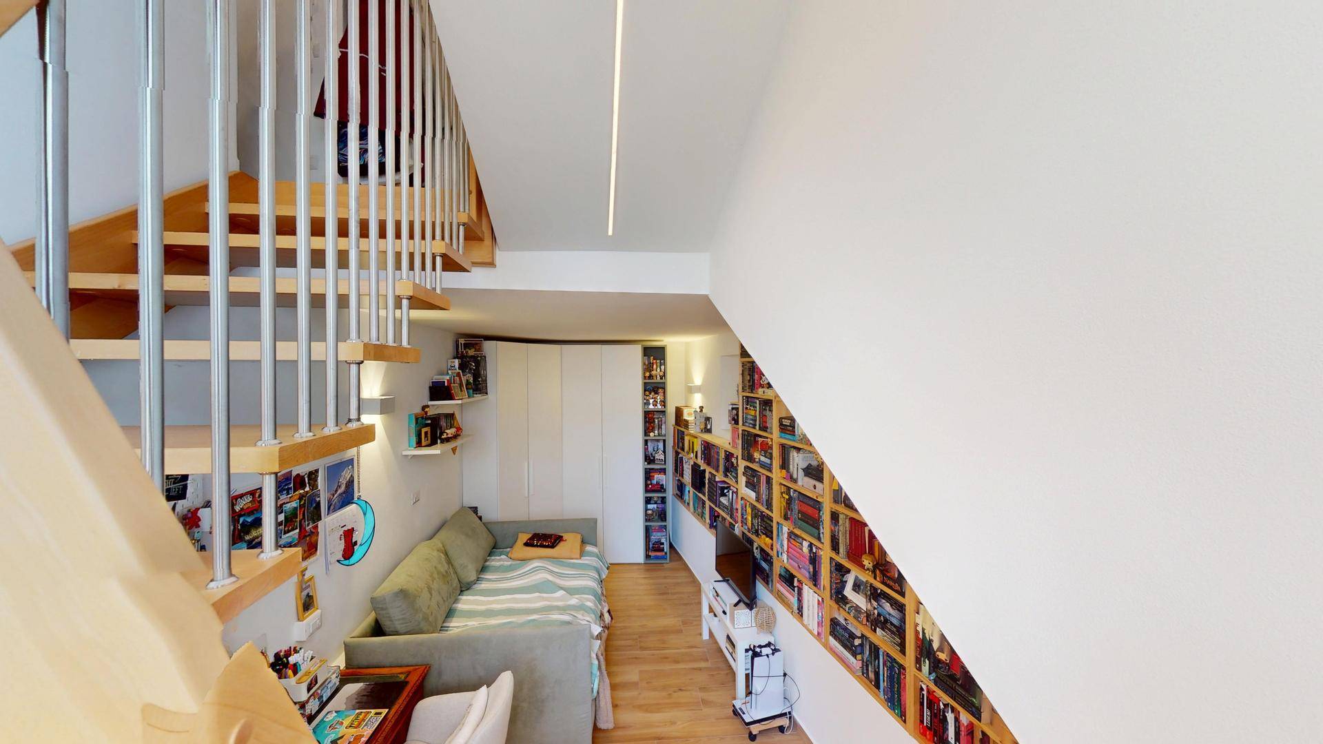 Wohnbereich mit integriertem Bücherregal, Sofa und Zugang zur Treppe.
