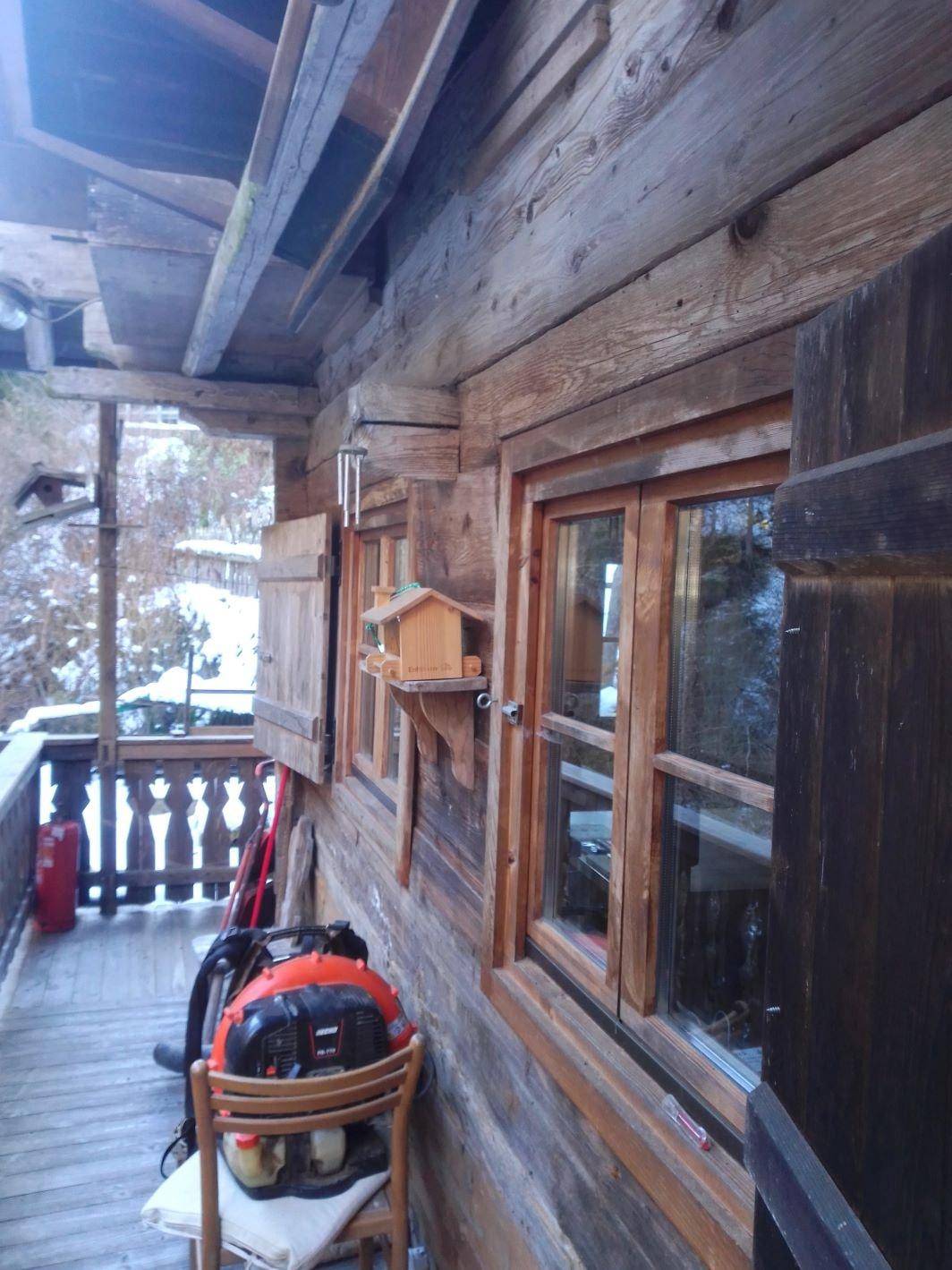Detailansicht der rustikalen Holzfassade mit Fenstern und einem Vogelhäuschen auf dem Balkon.