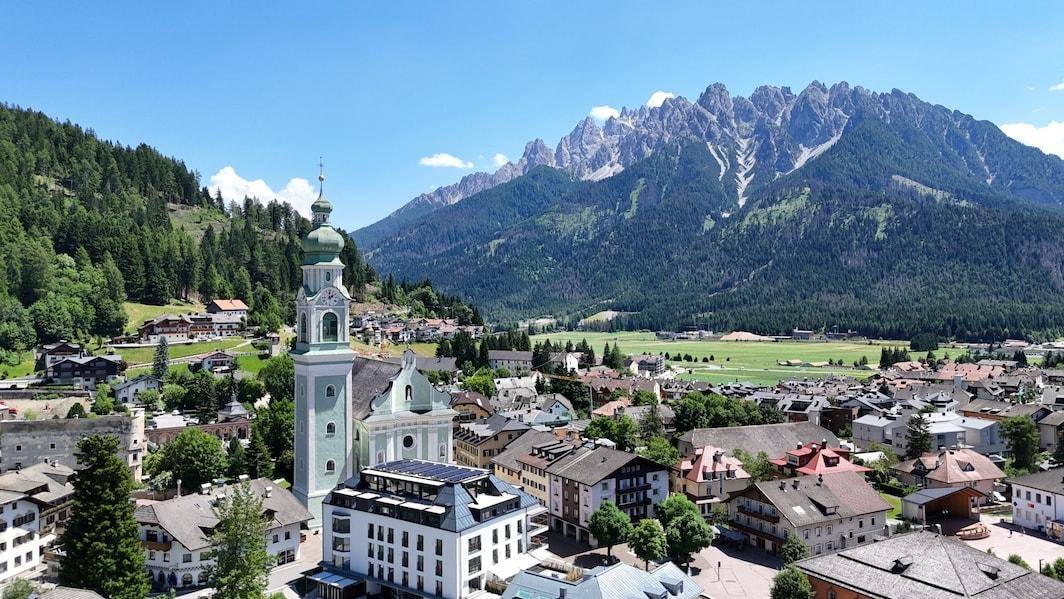 Weitläufiger Blick über eine charmante Alpenstadt mit Kirche und majestätischen Bergen im Hintergrund.