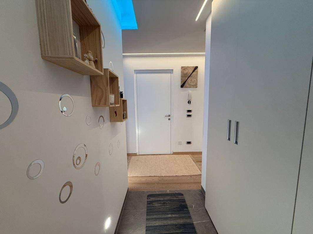 Heller Flur mit modernen Wanddekorationen, Holzboden und weißer Eingangstür.