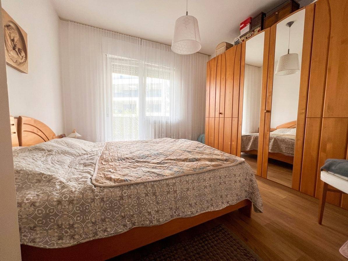 Helles Schlafzimmer mit Doppelbett, Holzschrank und Parkettboden.