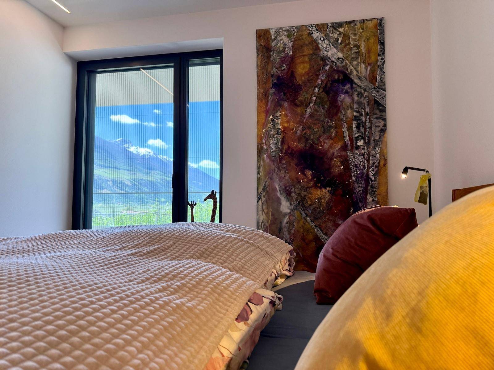 Schlafzimmer mit großem Bett, moderner Kunst und Fenster mit Blick auf die Berge.