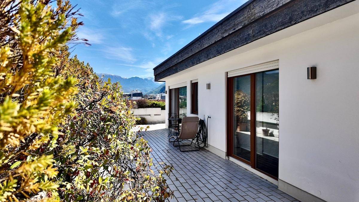 Geräumige gepflasterte Terrasse mit Liegestuhl und Blick auf die umliegende Berglandschaft.