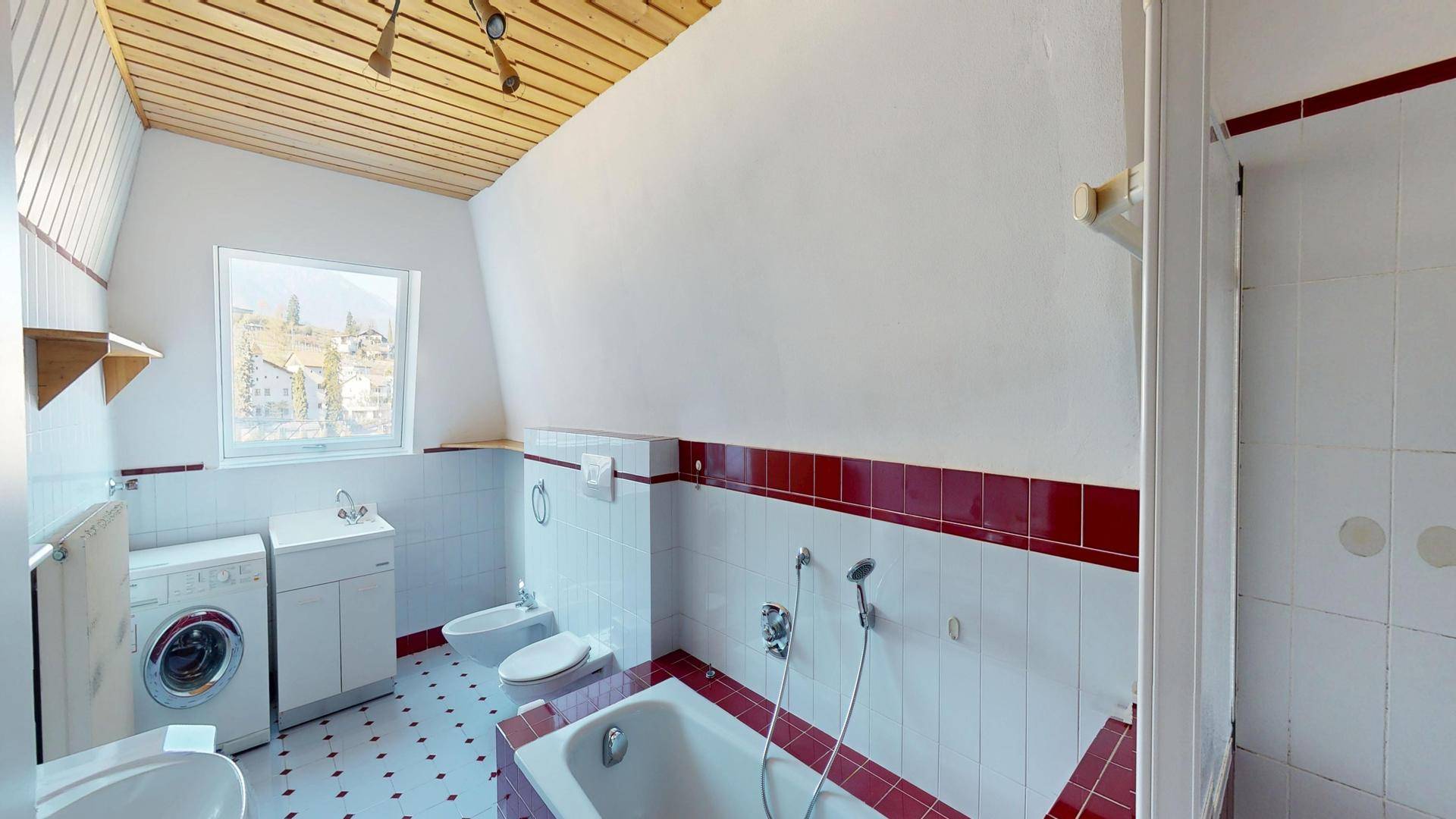 Badezimmer mit Badewanne, Bidet, Waschmaschine und Dachfenster mit Bergblick.