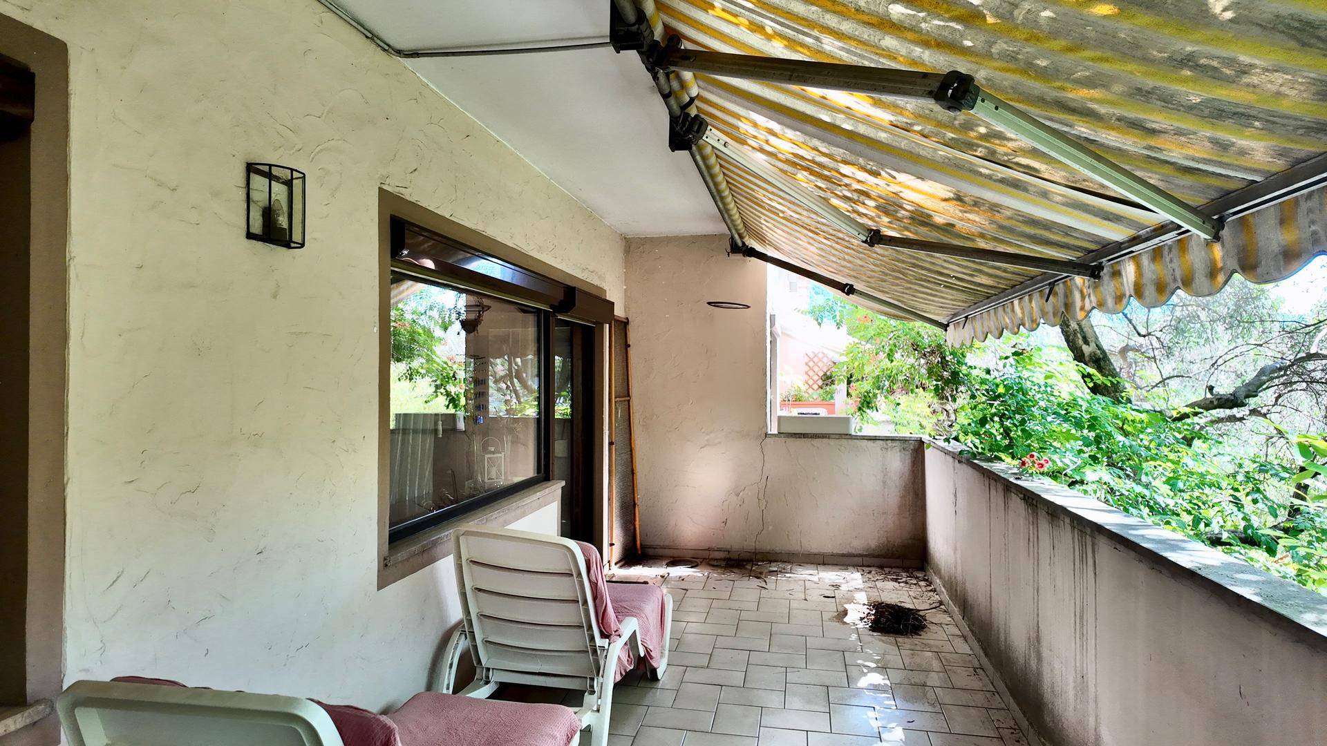 Balkon mit Fliesenboden, Markise und Blick auf die grüne Umgebung.