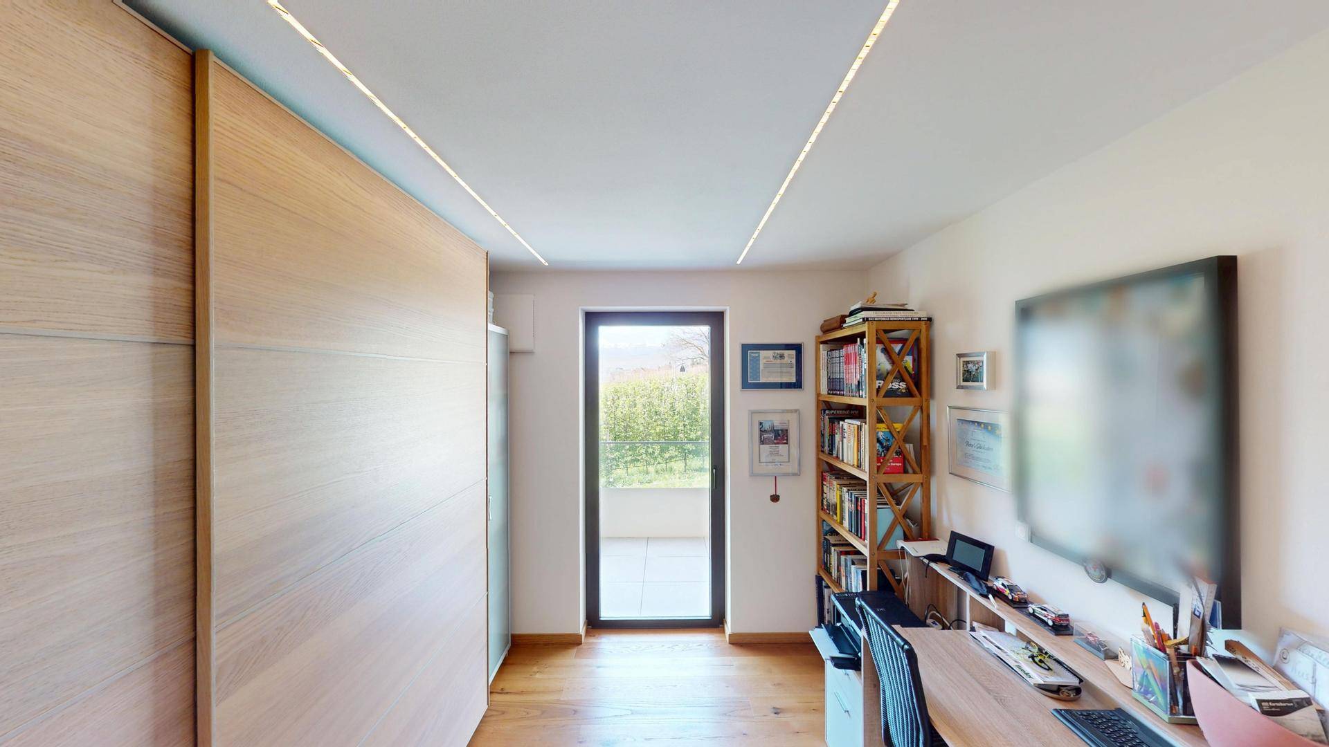 Helles Arbeitszimmer mit Schreibtisch, Bücherregal und Zugang zu einem Außenbereich.