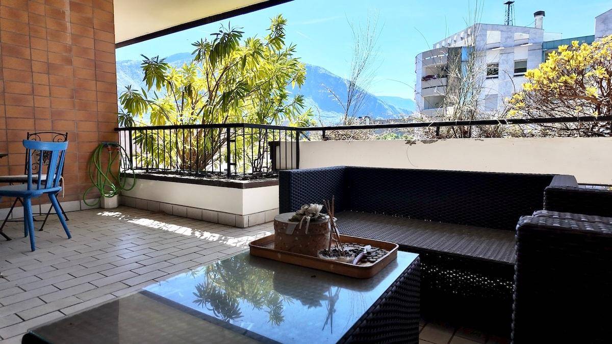 Überdachter Balkon mit Sitzgelegenheiten und weitem Blick auf die Berge und die Stadt.