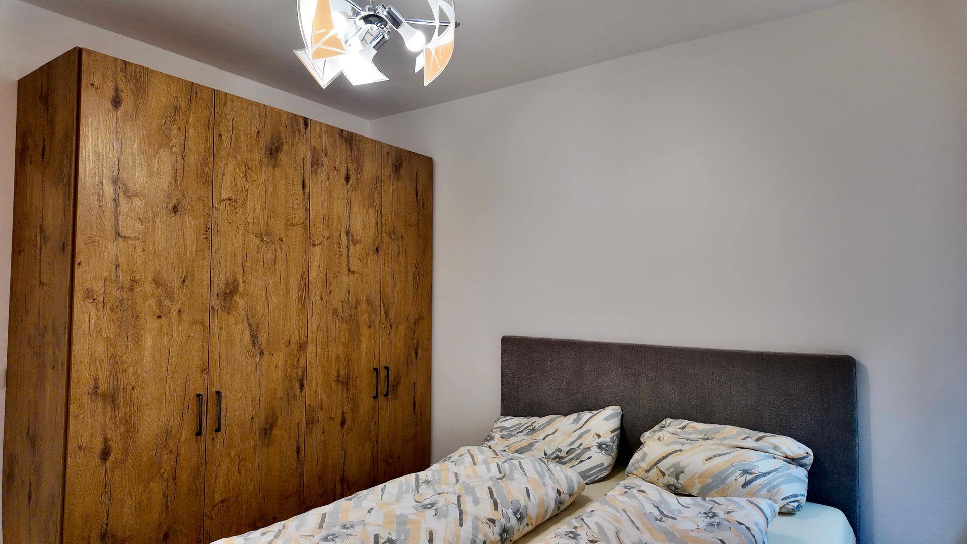 Schlafzimmer mit großem Kleiderschrank in Holzoptik und einem gemütlichen Bett mit Kopfteil.