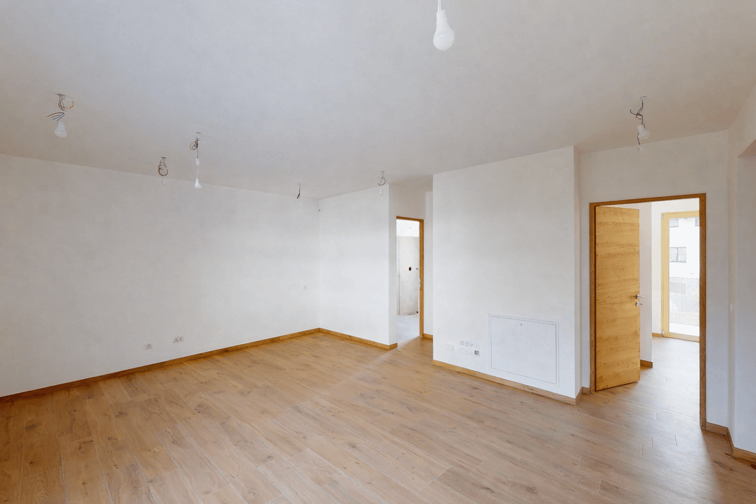 Geräumiger, unmöblierter Wohnbereich mit hellem Holzboden und mehreren Türöffnungen.