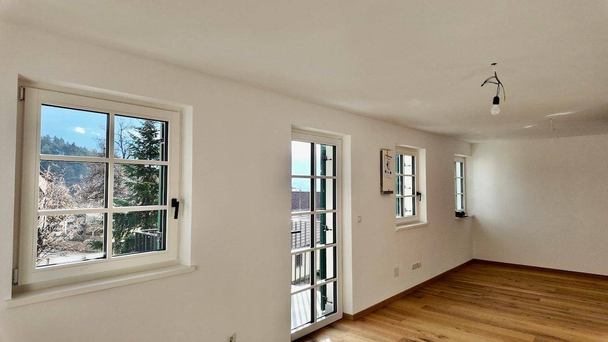Lichtdurchfluteter Raum mit Holzboden und Fenstern, die einen grünen Ausblick bieten.