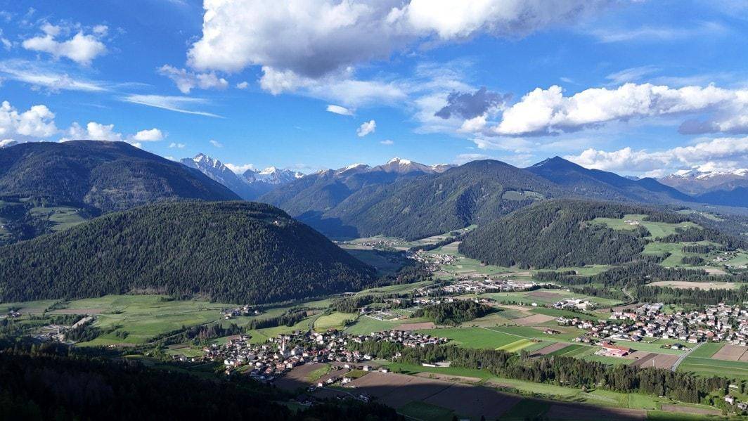 Panoramablick über ein weites Tal mit verstreuten Dörfern, umrahmt von bewaldeten Bergen und blauem Himmel.