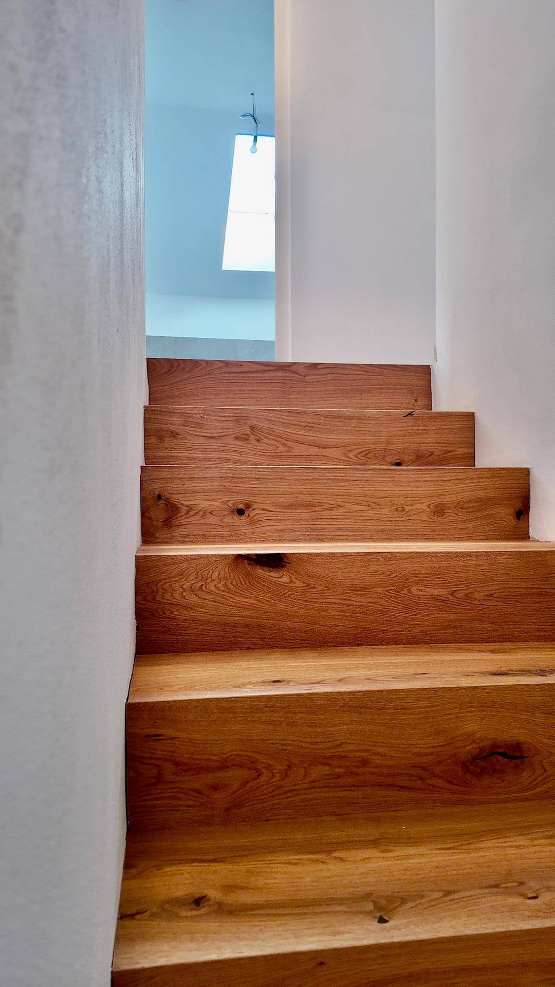 Detailaufnahme einer eleganten Holztreppe mit natürlicher Maserung, die in ein helles Obergeschoss führt.