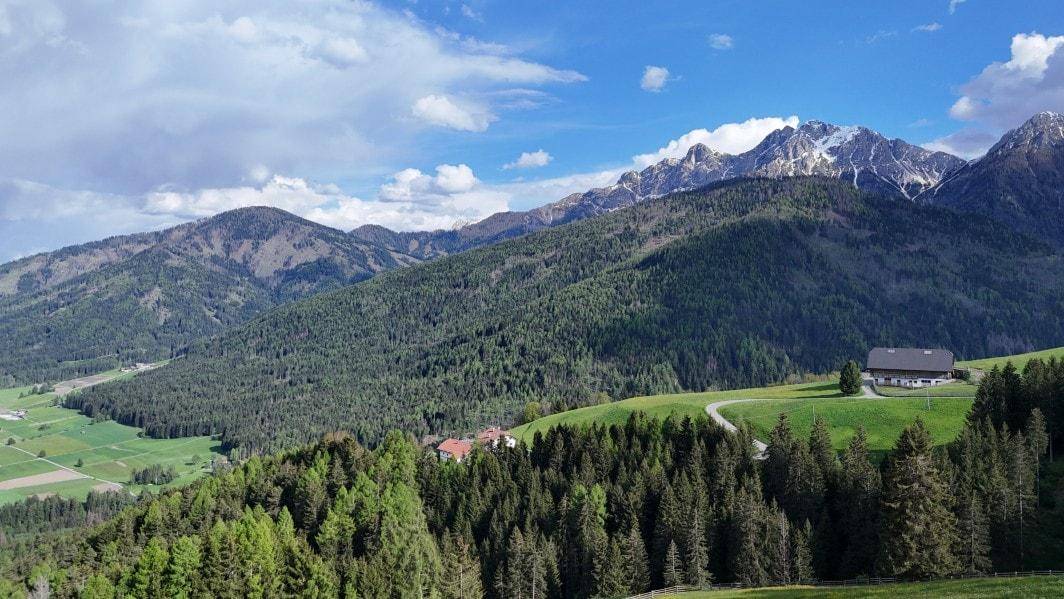 Malerische Bergkulisse mit schneebedeckten Gipfeln, dichten Wäldern und einem einzelnen Haus in der Ferne.