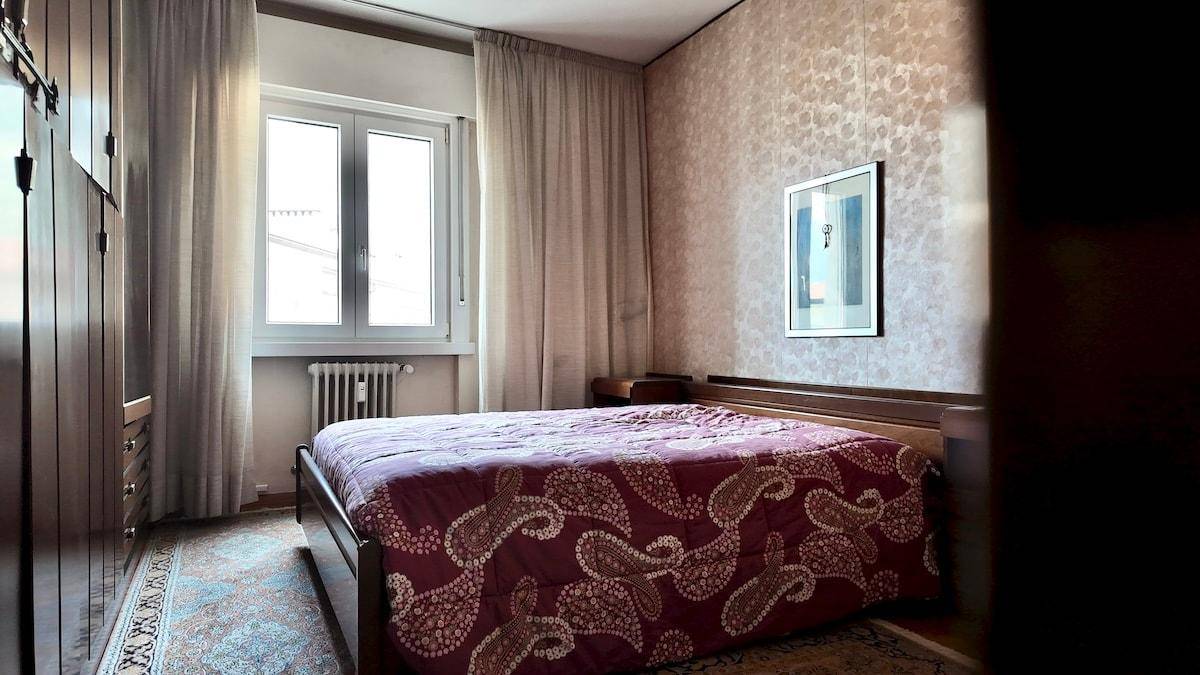 Schlafzimmer mit Doppelbett, gemusterter Tapete und Fenster mit Vorhängen.
