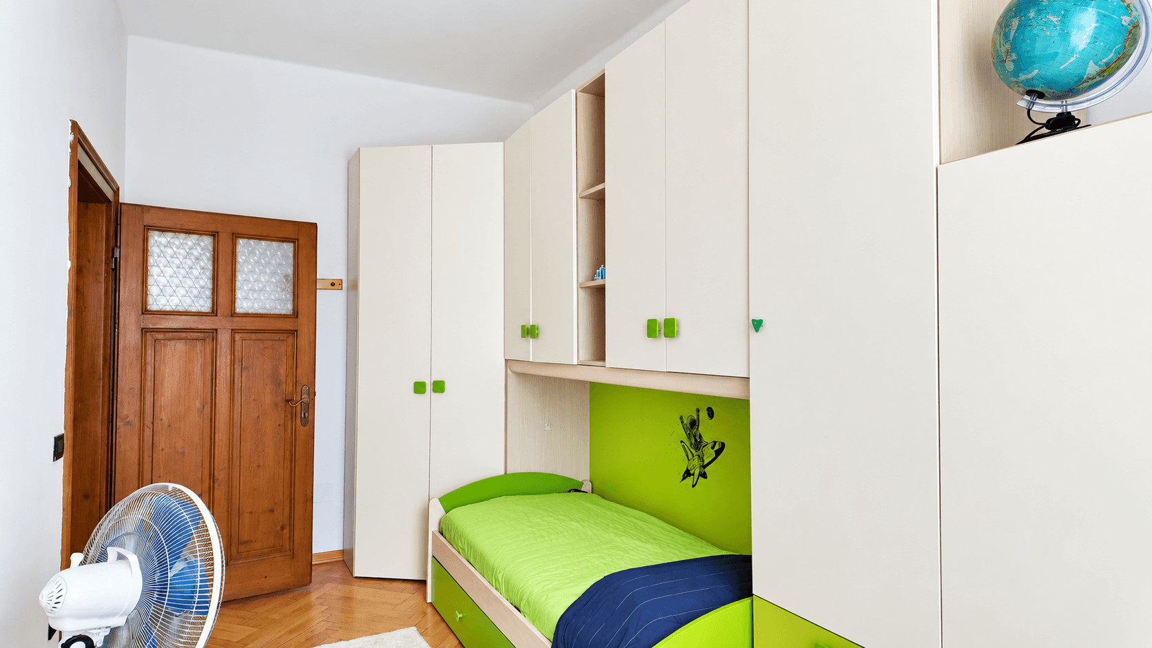Kinderzimmer mit grün-weißen Möbeln, Einzelbett und Holzschrank.