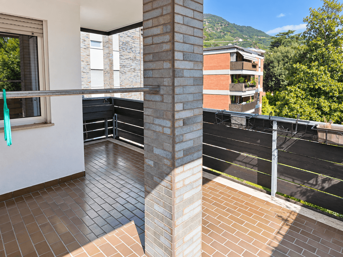 Geräumiger Balkon mit Fliesenboden, Ziegelsäule und Blick auf die umliegenden Gebäude.