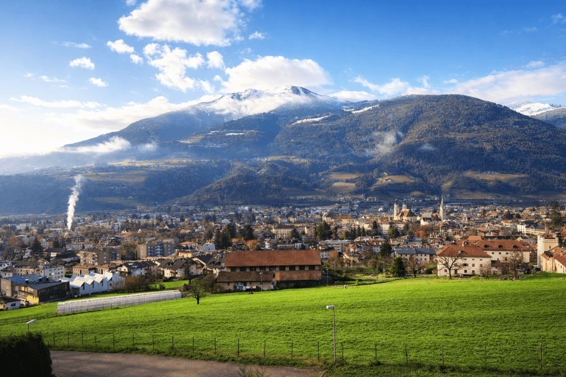 Weitläufiger Blick über eine Stadt im Tal, umgeben von grünen Hügeln und schneebedeckten Bergen.