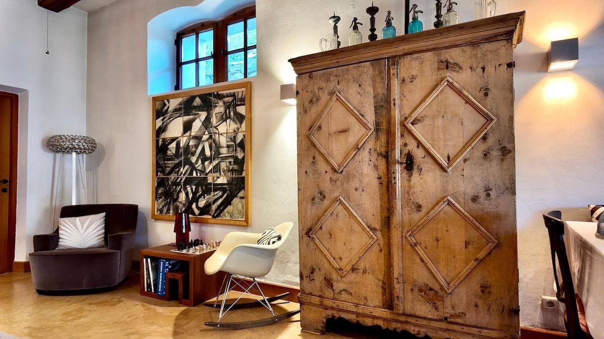 Wohnbereich mit einem großen, rustikalen Holzschrank, einem bequemen Sessel und einem Fenster mit viel Tageslicht.
