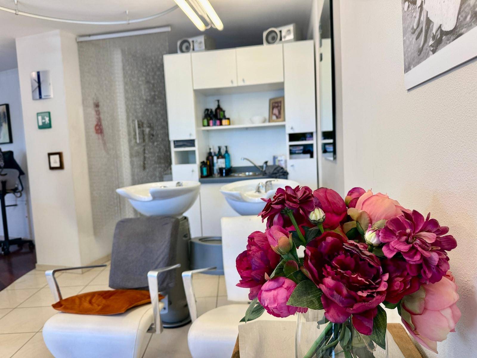 Bereich mit Waschbecken und Stühlen im Salon, dekoriert mit einem frischen Blumenstrauß.