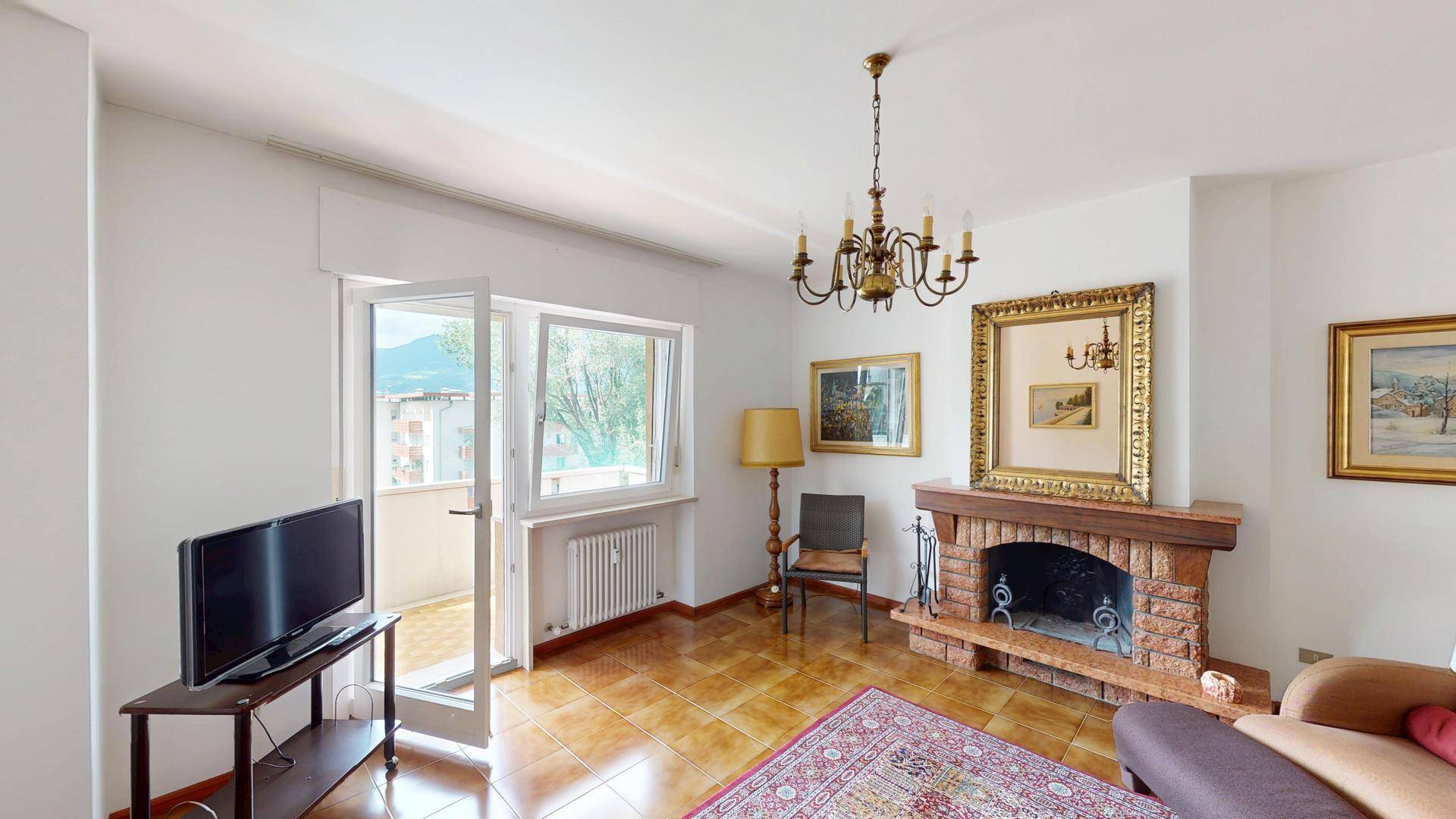 Helles Wohnzimmer mit traditionellem Kamin, Fliesenboden und Zugang zum Balkon mit Bergblick.