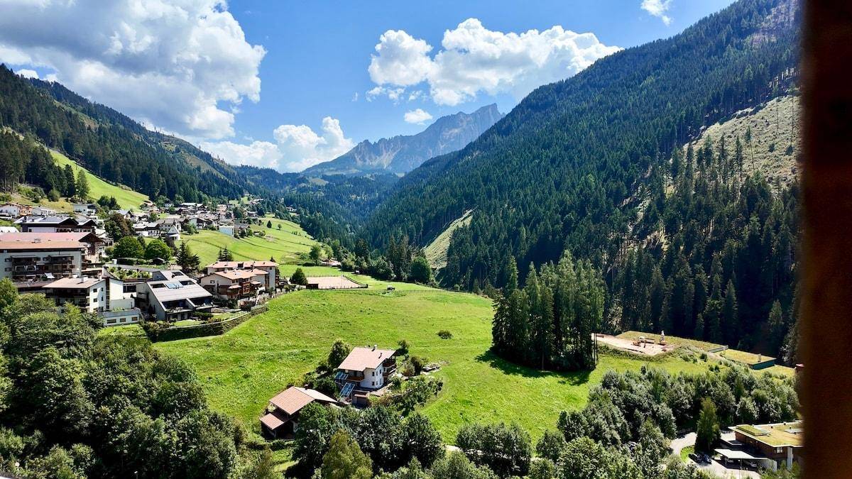 Malerischer Panoramablick auf ein grünes Tal mit bewaldeten Bergen und einem charmanten Dorf.