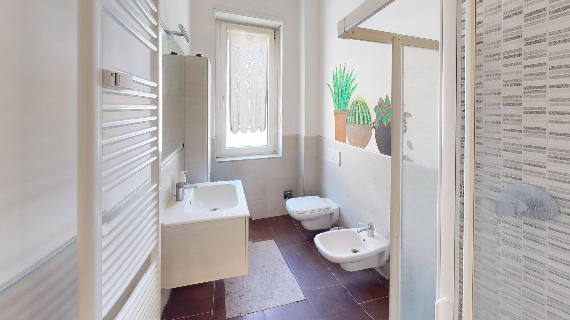 Helles Badezimmer mit Fenster, Dusche, Bidet und beheiztem Handtuchhalter.