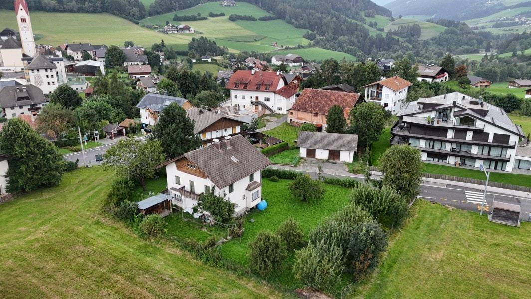 Luftaufnahme des Hauses mit gepflegtem Garten und Blick auf das umliegende Dorf und die Berge.