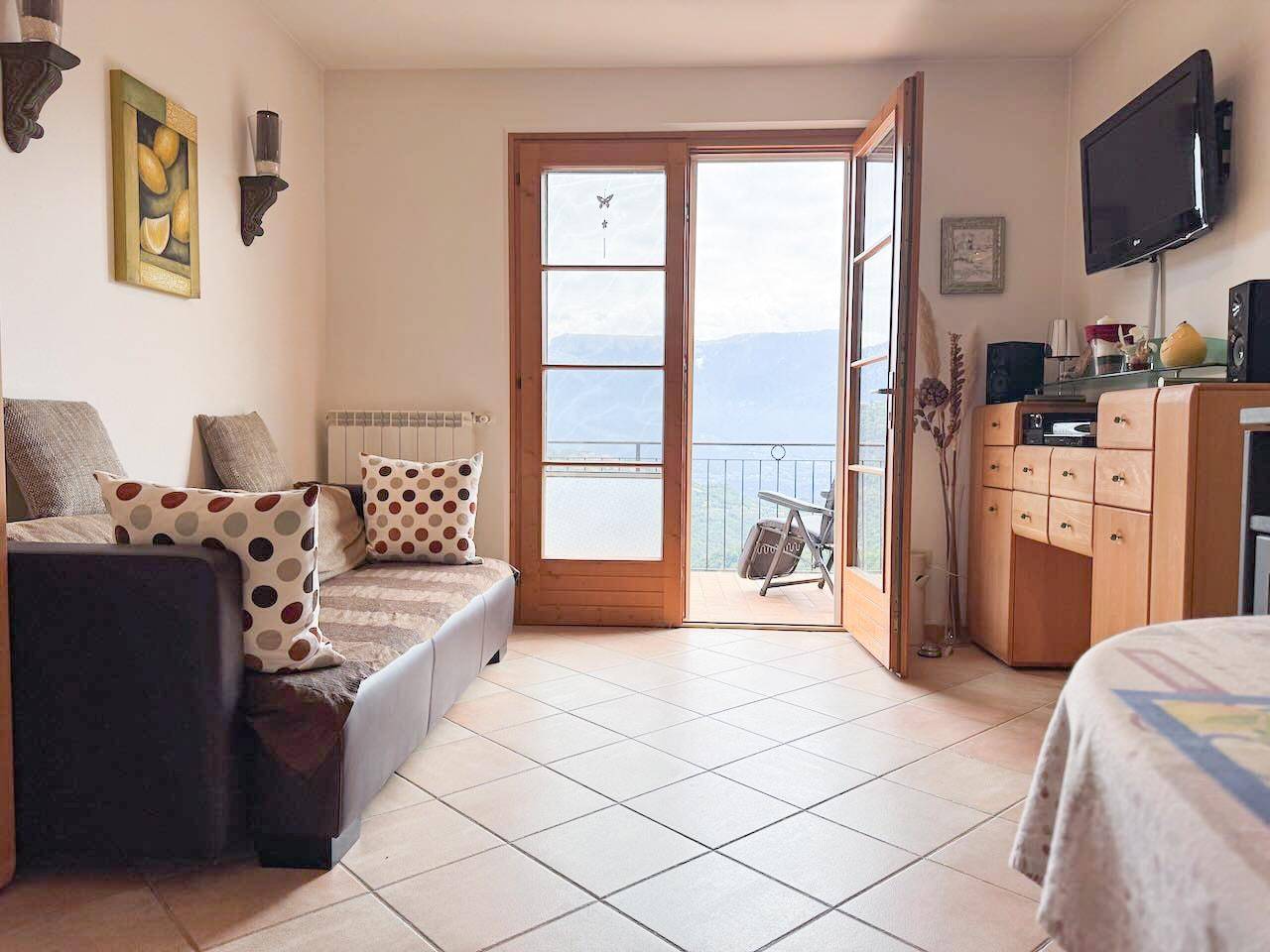 Gemütliches Wohnzimmer mit Fliesenboden und Zugang zu einem Balkon mit Bergblick.