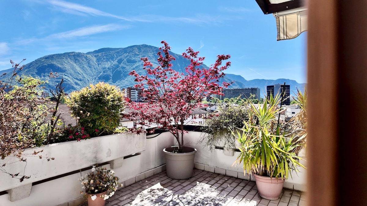 Sonniger Terrassenbereich mit Pflanzen und weitem Blick auf die Berge und die Stadt.