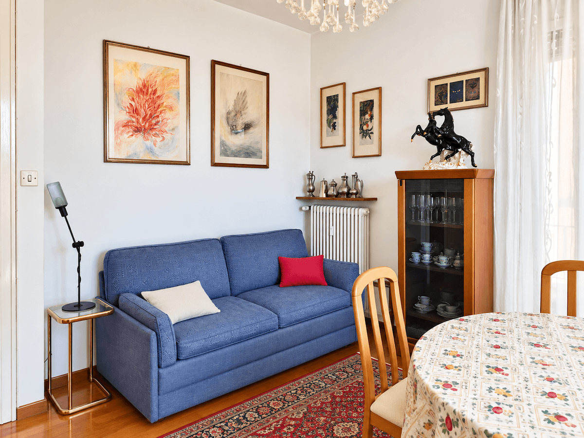 Heller Wohn- und Essbereich mit blauem Sofa, Esstisch und traditionellen Kunstwerken an den Wänden.