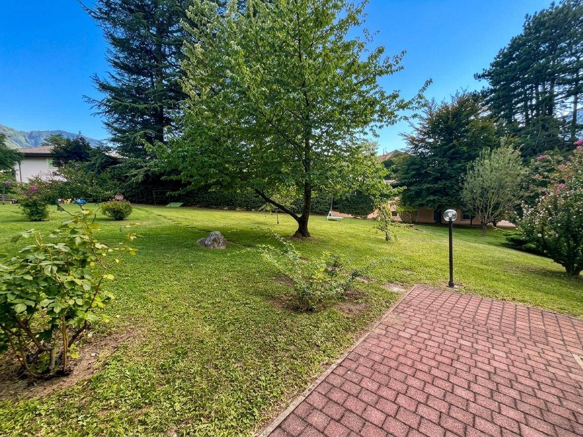 Großer, gepflegter Garten mit Rasenfläche, Bäumen und einem gepflasterten Weg.