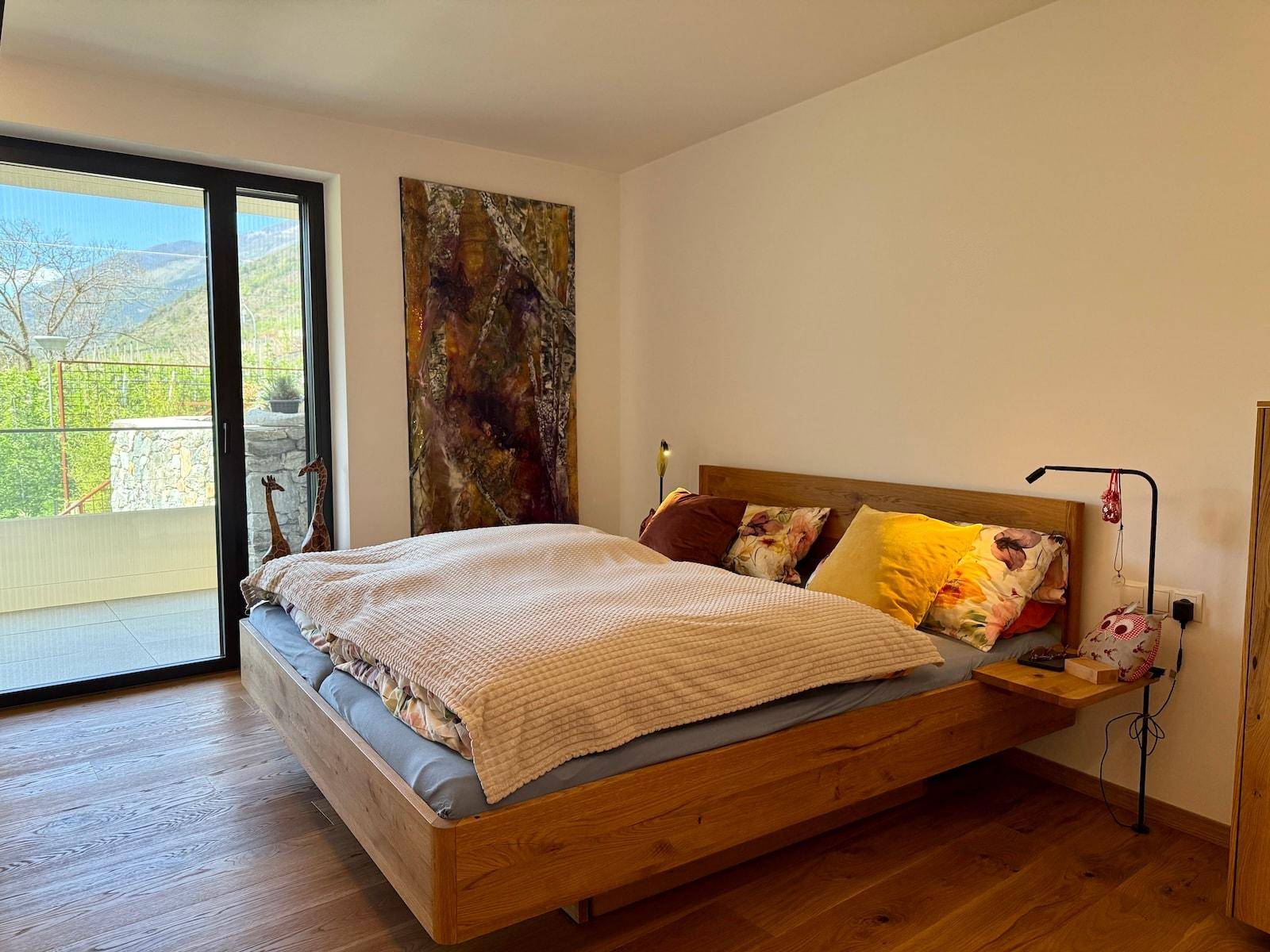 Helles Schlafzimmer mit Holzbett und Zugang zu einem Außenbereich mit Bergblick.