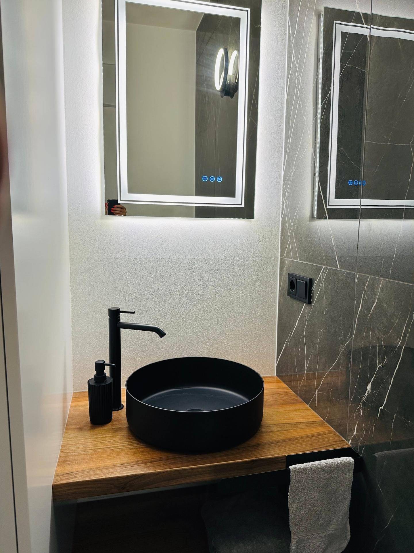 Modernes Gäste-WC mit rundem Aufsatzwaschbecken und beleuchtetem Spiegel.
