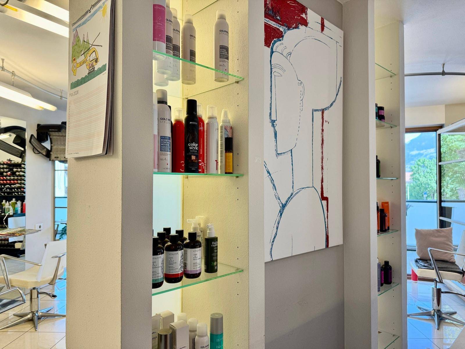Produktregal mit verschiedenen Haarpflegeprodukten und einem modernen Kunstwerk im Salon.