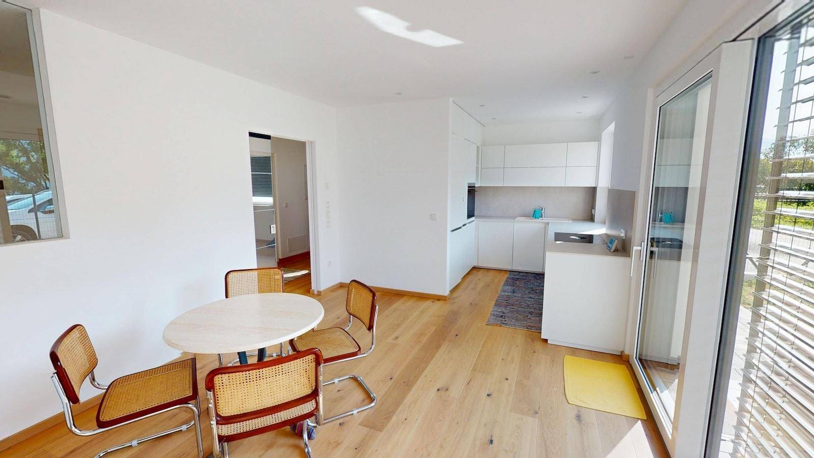 Geräumiger Wohn-Essbereich mit offener Küche, Holzboden und viel Tageslicht durch große Fenster.
