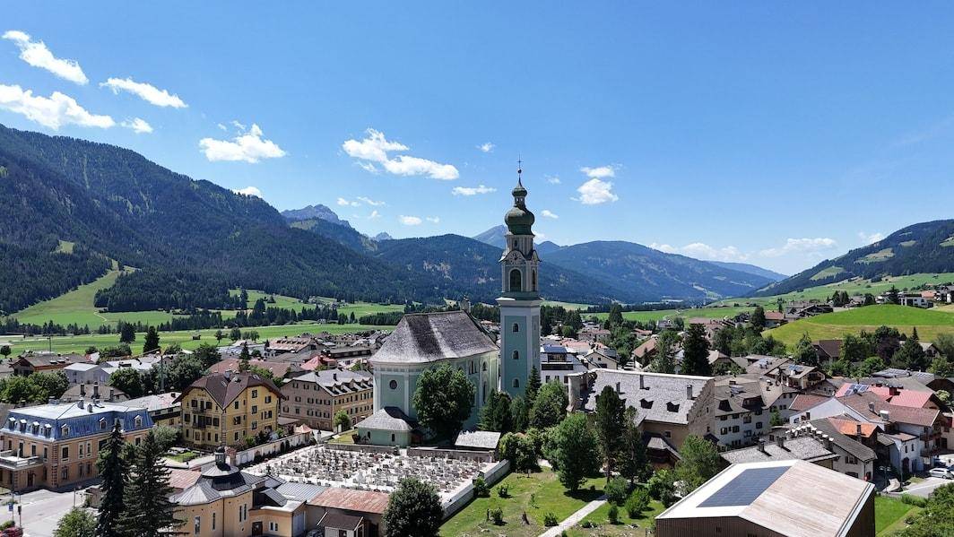 Idyllische Alpenlandschaft mit einem Dorf im Tal, umgeben von sanften Hügeln und Bergen.