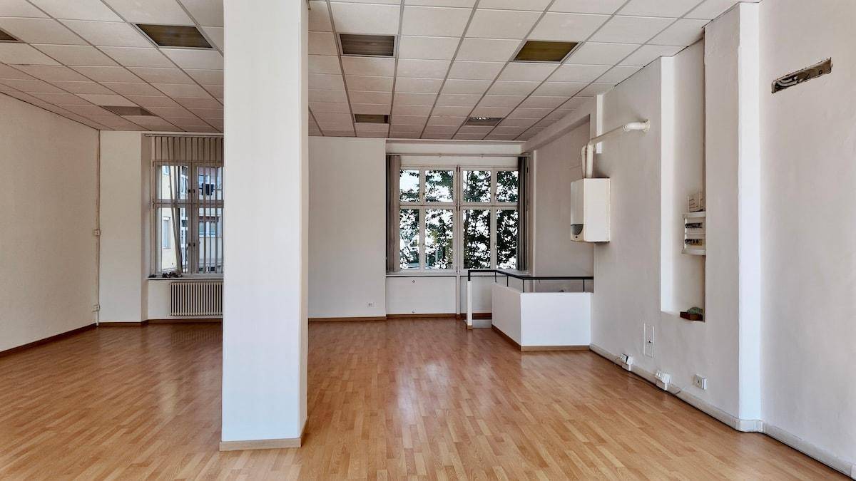 Leerer Büroraum mit Holzfußboden, weißen Wänden und Fenstern mit Blick ins Grüne.