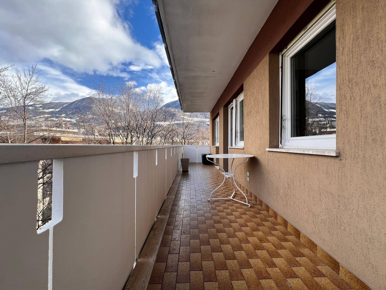 Langer Balkon mit Fliesenboden und beeindruckendem Blick auf die schneebedeckten Berge.