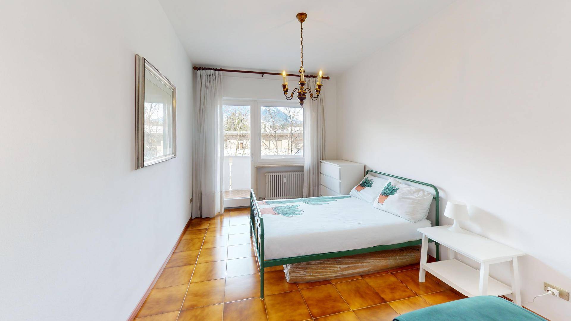 Helles Schlafzimmer mit Einzelbett, Fliesenboden und Balkonzugang.